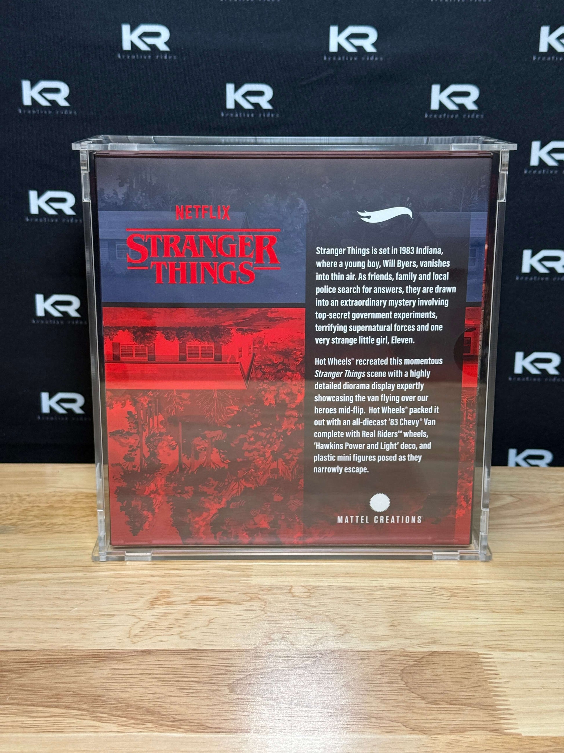 A Stranger Things collectible case featuring the back cover art, displayed on a light wood surface against a black background with repeating 'KR' logos.